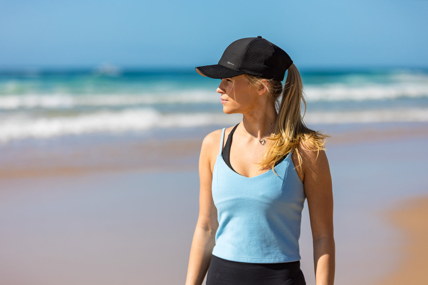 Scenic image capturing a runner wearing the Onpeak Performance Cap while sprinting along a sunlit beach. The cap's black design harmonizes with the natural surroundings, and its advanced features, including moisture-wicking, UV protection, antimicrobial sweatband, and buoyant visor core, are subtly highlighted. The runner's dynamic movement reflects the cap's perfect blend of style and performance for outdoor activities.