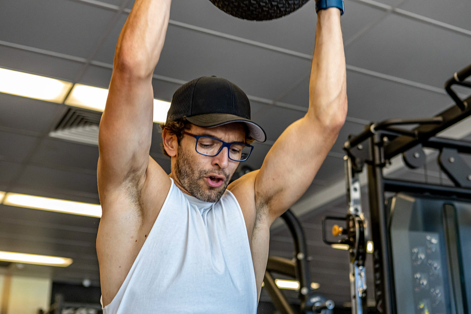 Image featuring a person wearing the Onpeak Performance Cap in a gym setting. The cap effortlessly complements the gym attire, showcasing its sleek black design and highlighting its performance features, including moisture-wicking, UV protection, antimicrobial sweatband, and buoyant visor core. The individual's focused demeanor underscores the cap's suitability for intense workouts and active fitness routines.